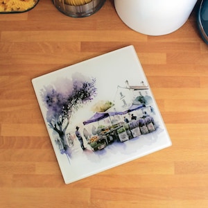 May include: A watercolour painting of a market scene with a purple awning, fresh produce, and people shopping. The painting is on a white background with a light blue sky and a green tree.