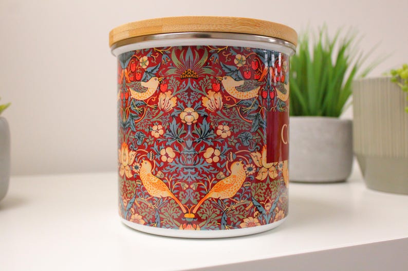 May include: A ceramic canister with a wooden lid features a colorful floral and bird pattern. The pattern includes red, blue, green, yellow, and white colors. The canister is labeled "Coffee".