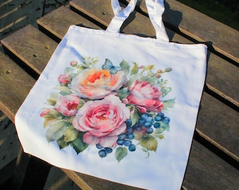 May include: White tote bag featuring a floral design with pink, peach, and white roses, green leaves, and blue berries. A blue butterfly is perched on one of the roses.