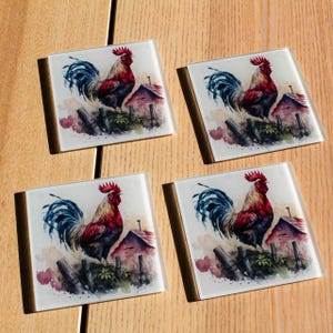 May include: Set of four square glass coasters featuring a watercolour illustration of a cockerel standing on a fence with a red barn in the background. The cockerel has a red comb, blue and black feathers, and a white beak.