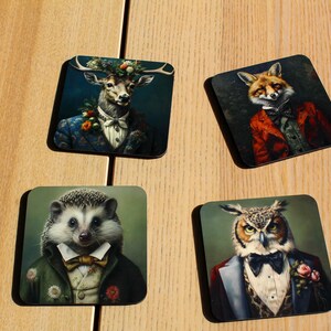 Può includere: Quattro sottobicchieri quadrati con diversi animali vestiti in abiti formali. I sottobicchieri sono realizzati in un materiale scuro e hanno una finitura lucida. Gli animali includono un cervo, una volpe, un riccio e un gufo.