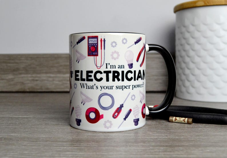 May include: White ceramic mug with a black rim and handle. The mug features a design of electrical tools and the text "I'm an Electrician. What's your super power?"
