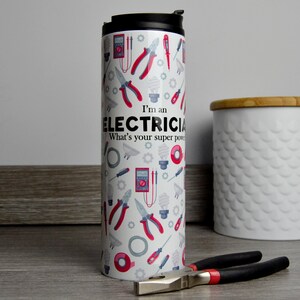 May include: White travel mug with a red and black design of electrician tools and the text "I'm an Electrician. What's your superpower?"