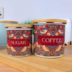 May include: Two ceramic canisters with bamboo lids, one labeled "Sugar" and the other "Coffee". Both canisters feature a colorful floral and bird pattern.