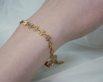 May include: A gold-colored bracelet featuring a daisy chain design. Each daisy has a turquoise center. The bracelet is worn on a wrist, showcasing its delicate floral pattern and bright color. The bracelet is a charming piece of jewelry.