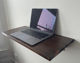 Può includere: Uno scaffale a parete in legno marrone scuro montato su una parete bianca con un computer portatile argentato sopra lo scaffale.