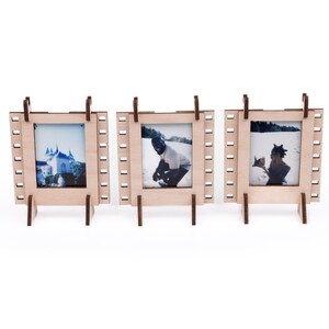 Può includere: Tre cornici per foto in legno con un design a pellicola. Ogni cornice contiene una foto diversa. Le cornici sono in piedi su una superficie bianca.