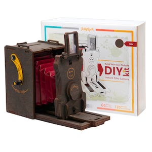 May include: A wooden DIY pinhole camera kit with 65 pieces and a build time of 120 minutes. The camera is brown with a red bellows and a yellow winding knob. The box is white with the text "Jollylook" and "Build Your Own Pinhole DIY Kit Instant Film Camera".