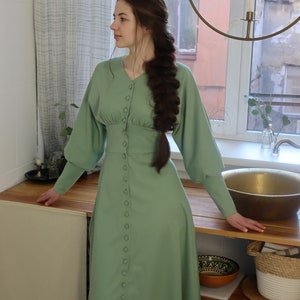 May include: A sage green midi dress with long sleeves and a button-up front. The dress has a fitted bodice and a flowy skirt.