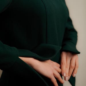 May include: A dark green dress with long sleeves and a v-neck. The sleeves have a wide cuff that is folded back.