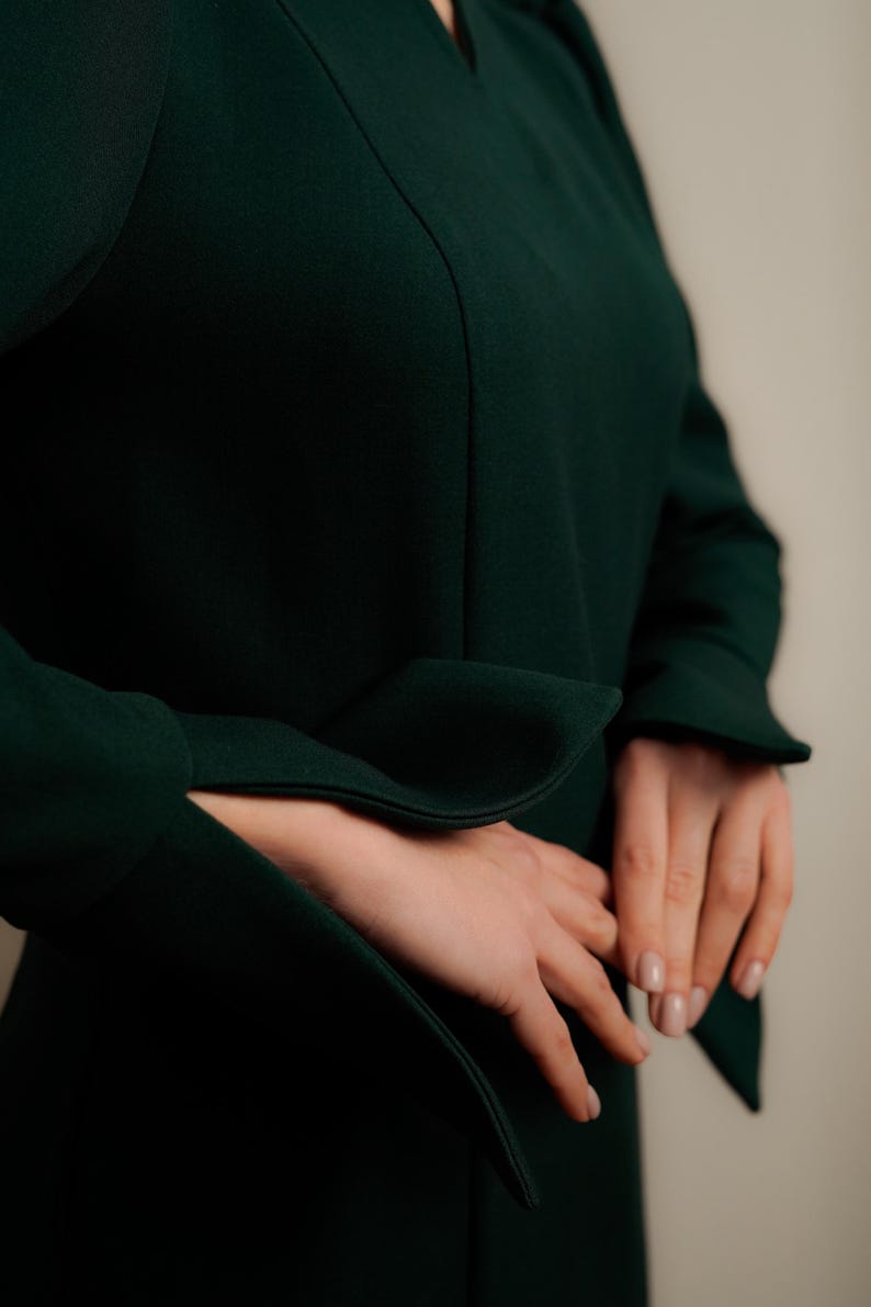 May include: A dark green dress with long sleeves and a v-neck. The sleeves have a wide cuff that is folded back.