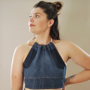 Puede incluir: Un top halter de mezclilla con escote fruncido y tirantes ajustables. El top es corto y tiene una tela de mezclilla azul con un ribete azul oscuro.