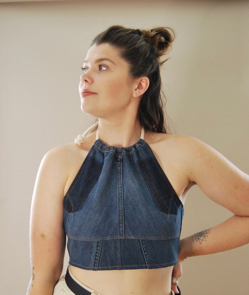 Puede incluir: Un top halter de mezclilla con escote fruncido y tirantes ajustables. El top es corto y tiene una tela de mezclilla azul con un ribete azul oscuro.