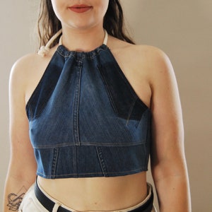 Puede incluir: Un top halter de mezclilla con un lazo de cuerda blanco. El top es corto y tiene un corpi&ntilde;o ajustado.