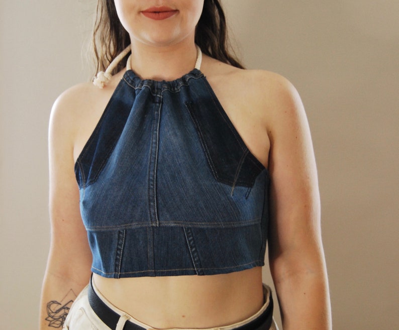 Puede incluir: Un top halter de mezclilla con un lazo de cuerda blanco. El top es corto y tiene un corpi&ntilde;o ajustado.
