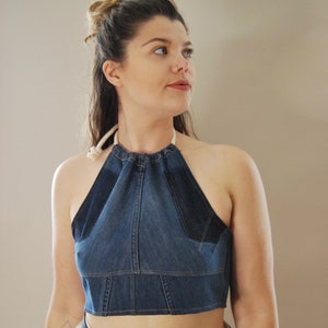Puede incluir: Un top halter de mezclilla con un escote fruncido y tirantes ajustables. El top es corto y est&aacute; hecho de tela de mezclilla azul.