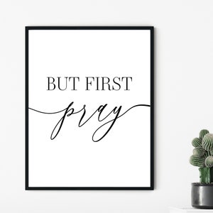 May include: Black and white printable wall art with the text "But First Pray" in a modern calligraphy font.