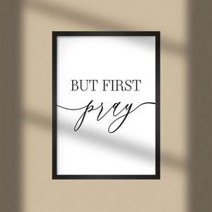 May include: A black framed print with white background and the text "BUT FIRST pray" in black cursive font.