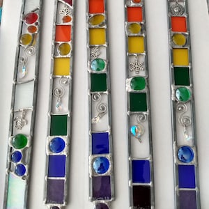 May include: Five stained glass suncatchers with a rainbow color scheme. Each suncatcher features a different design, including a snowflake, a butterfly, a turtle, a swirl, and a lion. The suncatchers are made with clear, red, orange, yellow, green, blue, and purple glass.
