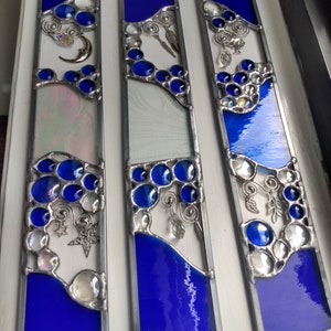 May include: Three stained glass panels with a blue and white design. Each panel features a crescent moon, stars, and a variety of glass beads and charms. The panels are framed in silver metal.