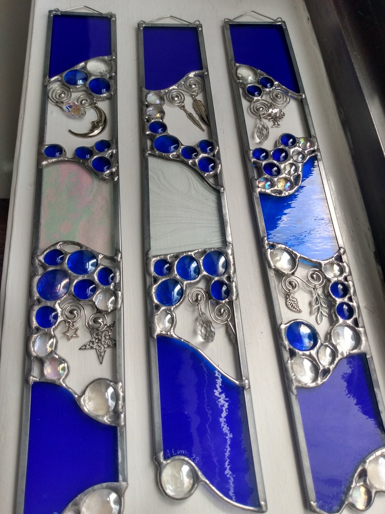 May include: Three stained glass panels with a blue and white design. Each panel features a crescent moon, stars, and a variety of glass beads and charms. The panels are framed in silver metal.