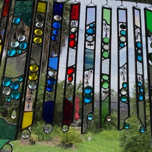 May include: A stained glass suncatcher with a variety of colors and designs. The suncatcher is made up of several individual pieces of glass that are joined together with lead. The glass is clear, blue, green, red, yellow, and white. The designs include circles, swirls, and butterflies.