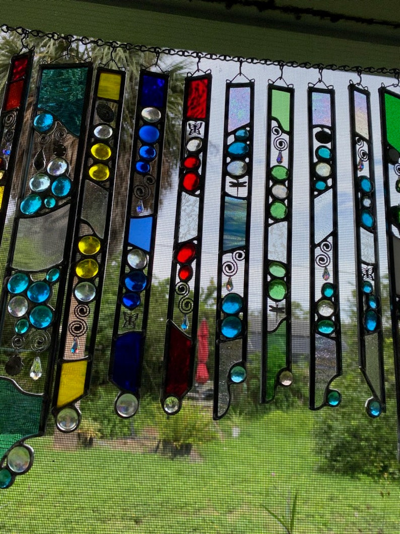 May include: A stained glass suncatcher with a variety of colors and designs. The suncatcher is made up of several individual pieces of glass that are joined together with lead. The glass is clear, blue, green, red, yellow, and white. The designs include circles, swirls, and butterflies.