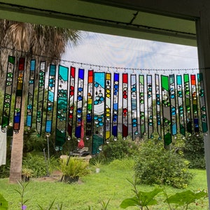 May include: A colorful stained glass suncatcher with a variety of colors and shapes, including blue, green, red, and yellow. The suncatcher is hanging in a window and is reflecting light.