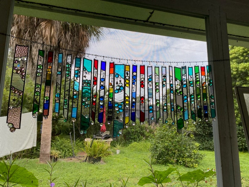 May include: A colorful stained glass suncatcher with a variety of colors and shapes, including blue, green, red, and yellow. The suncatcher is hanging in a window and is reflecting light.