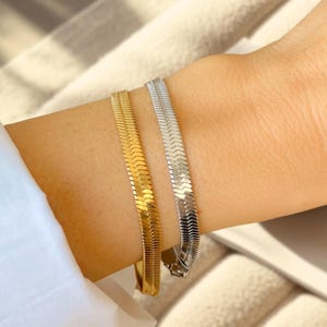 May include: Two gold and silver chain bracelets on a wrist. The bracelets are both snake chain style.