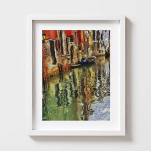 May include: A framed art print depicting a canal scene in Venice. The artwork features colorful buildings in shades of red, orange, and yellow reflected in the water. A small boat is visible in the canal.