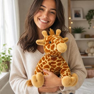 May include: A plush giraffe toy featuring a soft, brown and tan spotted pattern across its body, head, and neck. The stuffed animal has small ossicones on top of its head, a tuft of brown hair, and large, dark, round eyes with a light tan muzzle.