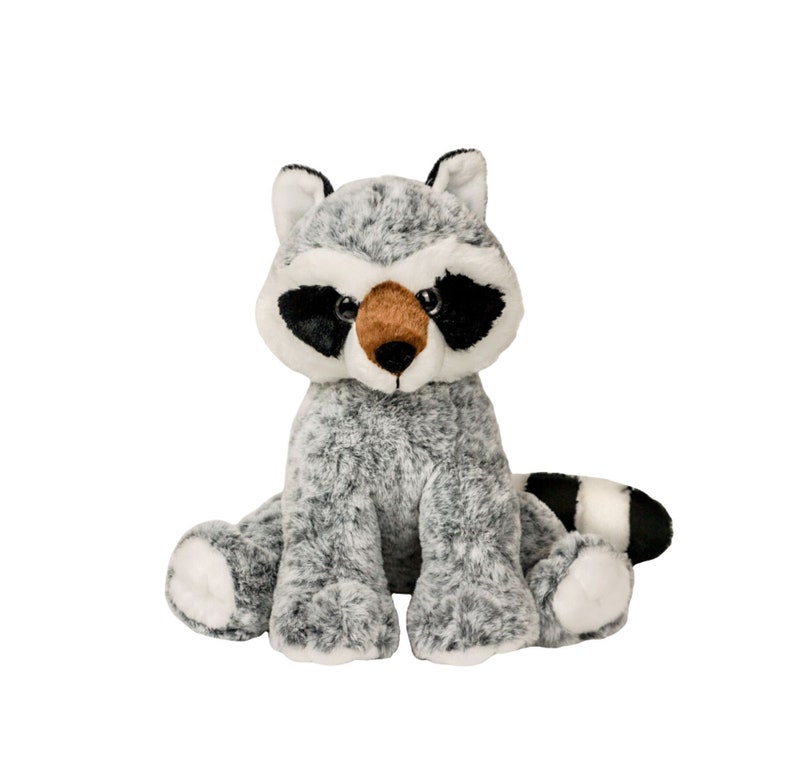 Puede incluir: Un juguete de peluche de mapache gris con ojos negros, nariz marr&oacute;n y cola rayada en blanco y negro. El mapache est&aacute; sentado con las patas delante de &eacute;l.