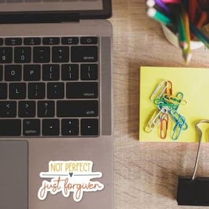 a laptop, a yellow sticky note, a binder clip, and a cup of colored pencils on a wooden surface.