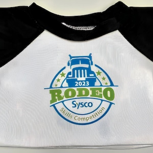 A white t-shirt with a black sleeve and a graphic design featuring a truck and the text "Rodeo Skills Competition" printed on it.