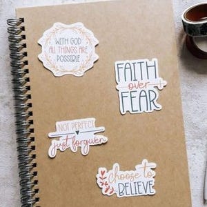 a brown spiral notebook with various stickers and a pen on a white surface.