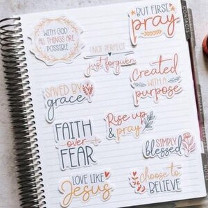 a spiral-bound notebook with various inspirational quotes and phrases written on its pages, along with a pen and some tape.