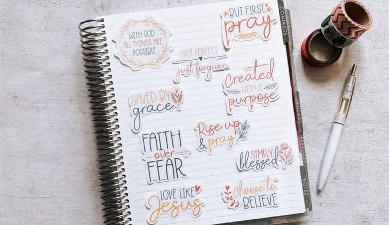 a spiral-bound notebook with various inspirational quotes and phrases written on its pages, along with a pen and some tape.