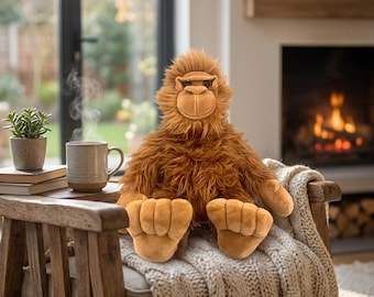 May include: A plush orangutan toy with shaggy brown fur, a tan face, and large hands and feet. The stuffed animal is seated upright, featuring a soft, textured appearance with detailed facial features and a neutral, friendly expression.