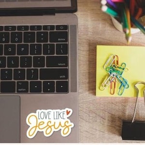 a laptop, a yellow sticky note, a binder clip, and a cup of colored pencils on a wooden surface.