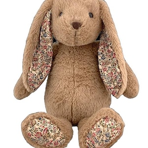 Puede incluir: Un conejito de peluche marr&oacute;n con orejas y patas con estampado floral. El conejito est&aacute; sentado con las patas juntas y las orejas levantadas.