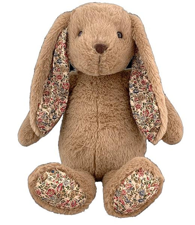 Puede incluir: Un conejito de peluche marr&oacute;n con orejas y patas con estampado floral. El conejito est&aacute; sentado con las patas juntas y las orejas levantadas.