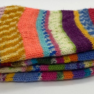 May include: Multicolored striped knitted socks folded in a stack. The socks are made of a soft, fuzzy yarn and feature a variety of colors, including pink, blue, green, yellow, and red.