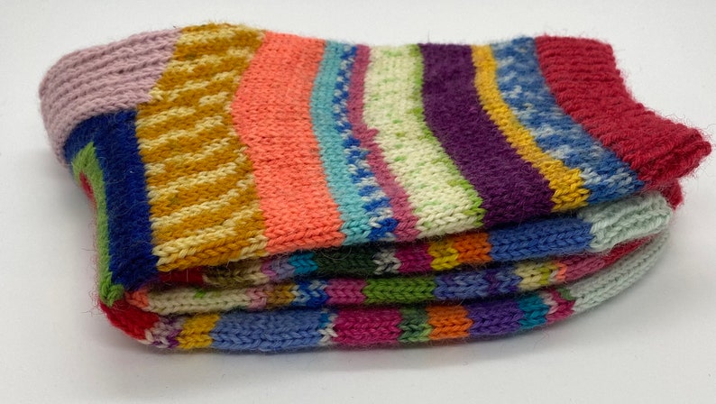 May include: Multicolored striped knitted socks folded in a stack. The socks are made of a soft, fuzzy yarn and feature a variety of colors, including pink, blue, green, yellow, and red.