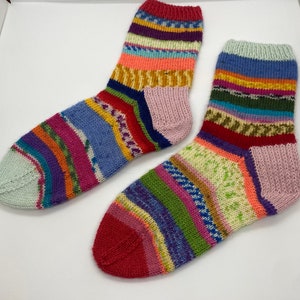 May include: A pair of colorful striped socks with a pink heel and toe. The socks are made of a soft, knitted fabric and feature a variety of colors, including red, blue, green, yellow, and purple.