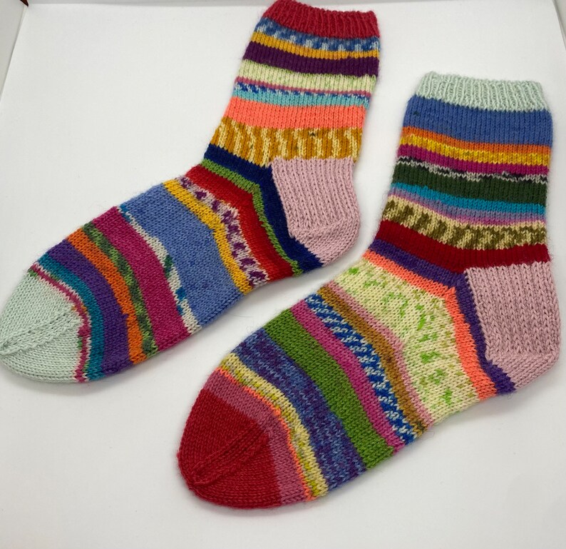 May include: A pair of colorful striped socks with a pink heel and toe. The socks are made of a soft, knitted fabric and feature a variety of colors, including red, blue, green, yellow, and purple.