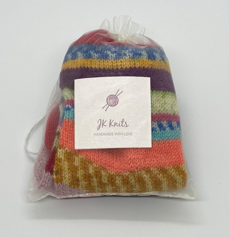May include: A colorful striped knitted item in a clear organza bag with a white tag that says "JK Knits handmade with love".