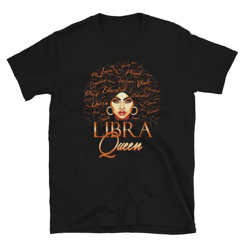 May include: Black t-shirt featuring a brown illustration of a woman's face with an afro hairstyle. The afro is made up of words describing a strong, confident woman. The words "LIBRA QUEEN" are written below the illustration.