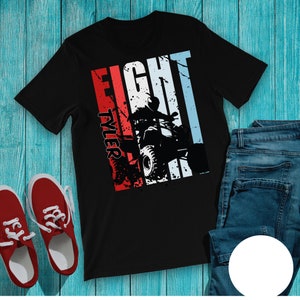 May include: Black t-shirt with a graphic of a person riding an ATV. The design includes the word "FIGHT" in white, red, and blue stripes, with the name "TYLER" in red. Red sneakers and blue jeans are also visible.