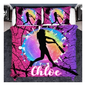 May include: A bedding set featuring a comforter and two pillowcases with a vibrant pink and purple cracked pattern. A central rainbow-colored circular graphic displays a black silhouette of a softball player swinging a bat with the text Eat, Sleep, Change, Repeat and the name Chloe in white script.